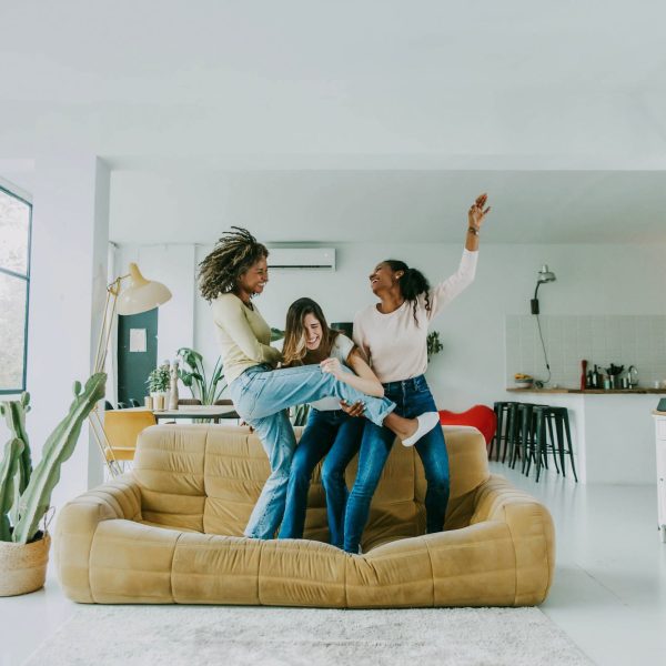 Diverse group of female friends enjoying party and laughing together - Women friends having fun at home dancing on the couch - Happy lifestyle and friendship concept